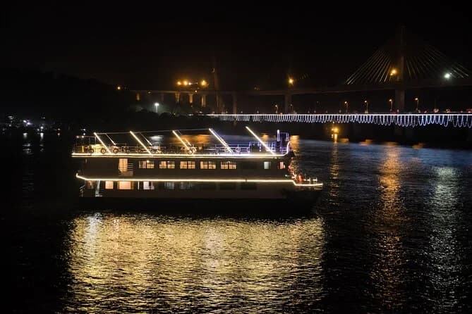 Lit cruise boat at night with the illuminated cable-stayed bridge behind